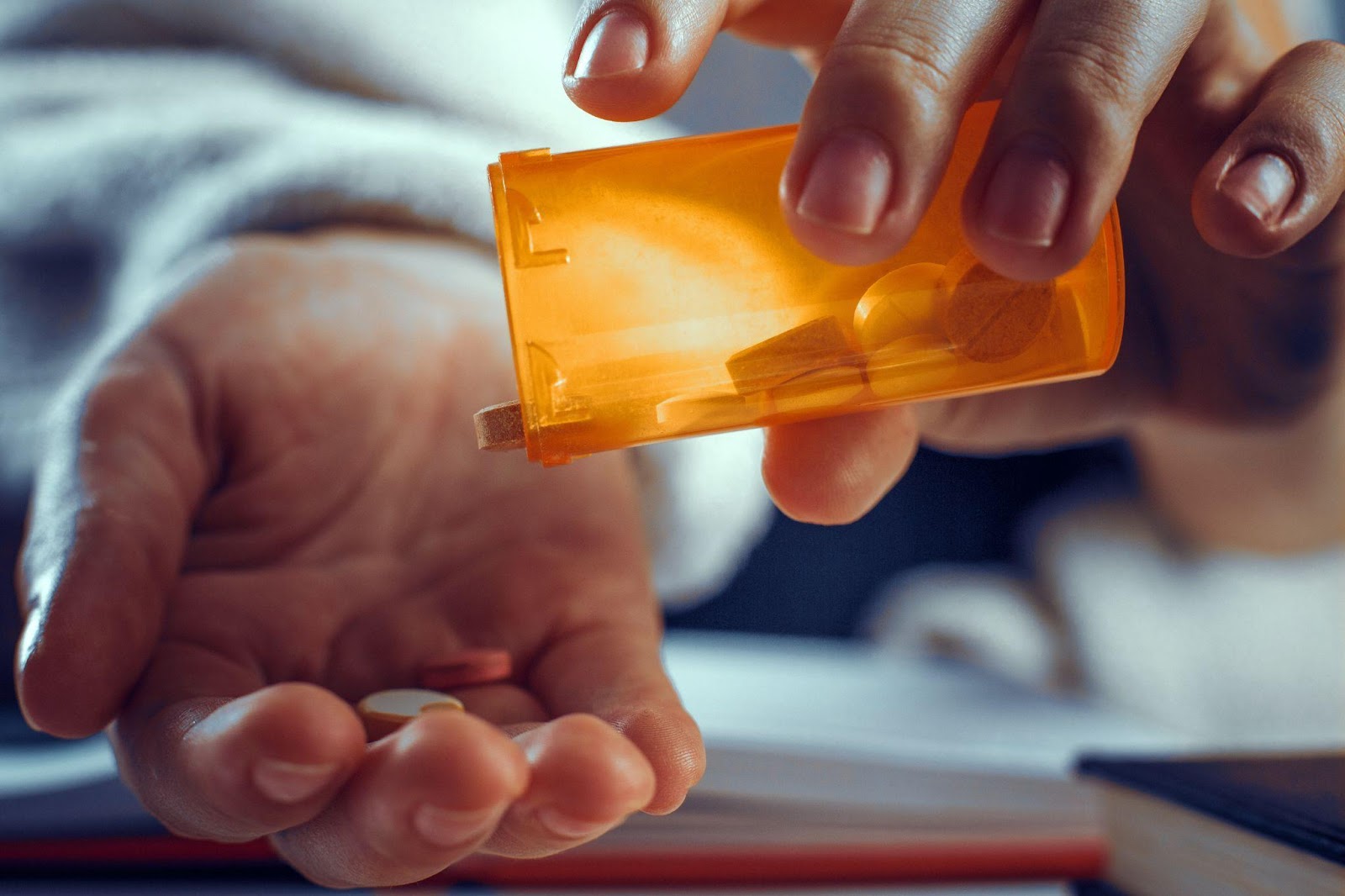 A hand dropping pills from a bottle, illustrating the serious consequences of possessing a controlled substance in Alabama and potential felony charges.