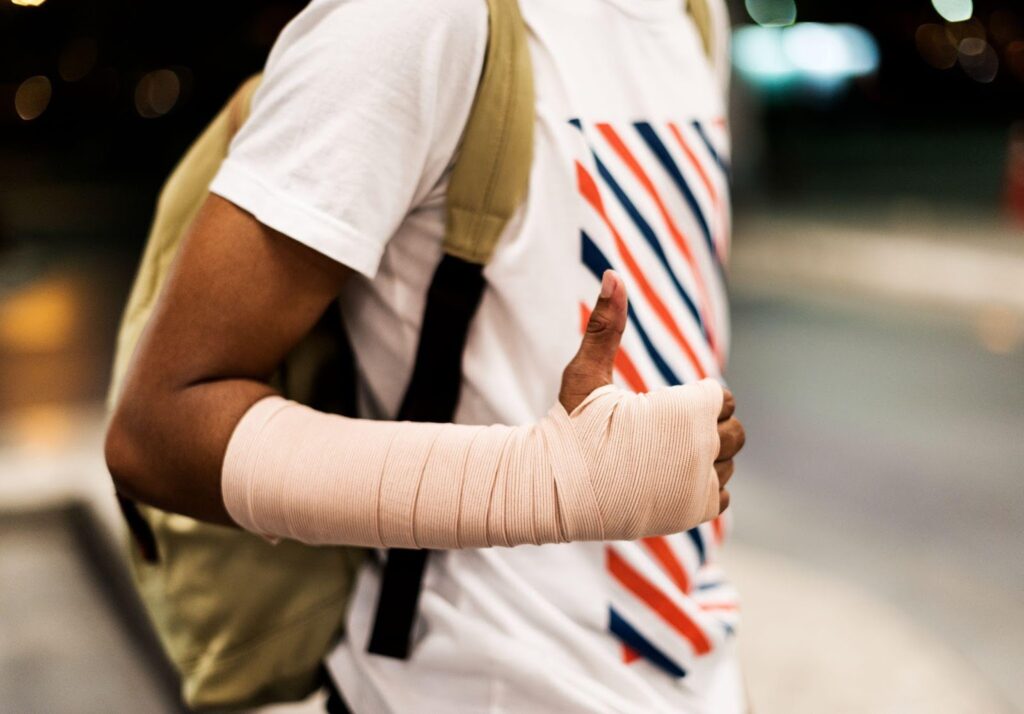 A young man with a bandaged arm gives a thumbs-up while carrying a backpack. This image reflects the challenges and resilience often experienced after a personal injury.