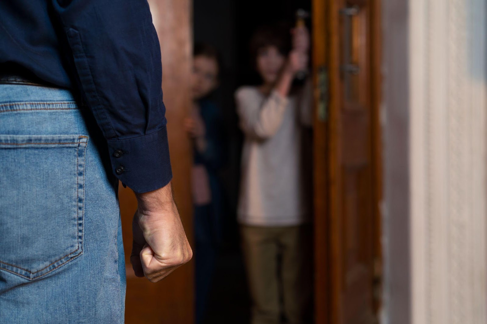 A tense scene showing a clenched fist in the foreground with two frightened children in the background inside a home. This image brings to light the gravity of domestic issues, such as abuse, while raising a question: what is the punishment for adultery in Alabama? Understanding the state's moral laws can help clarify their implications.