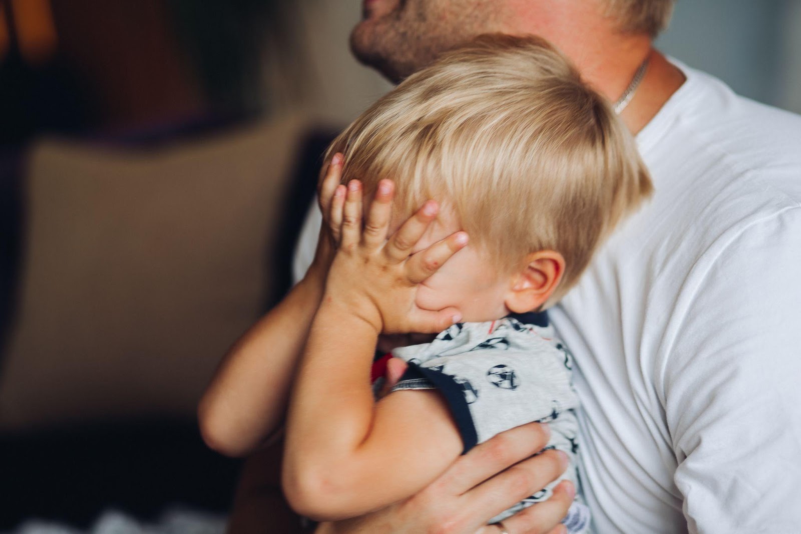 Father holding a young blond child who is covering his face with his hands, illustrating the emotional aspects of custody cases.