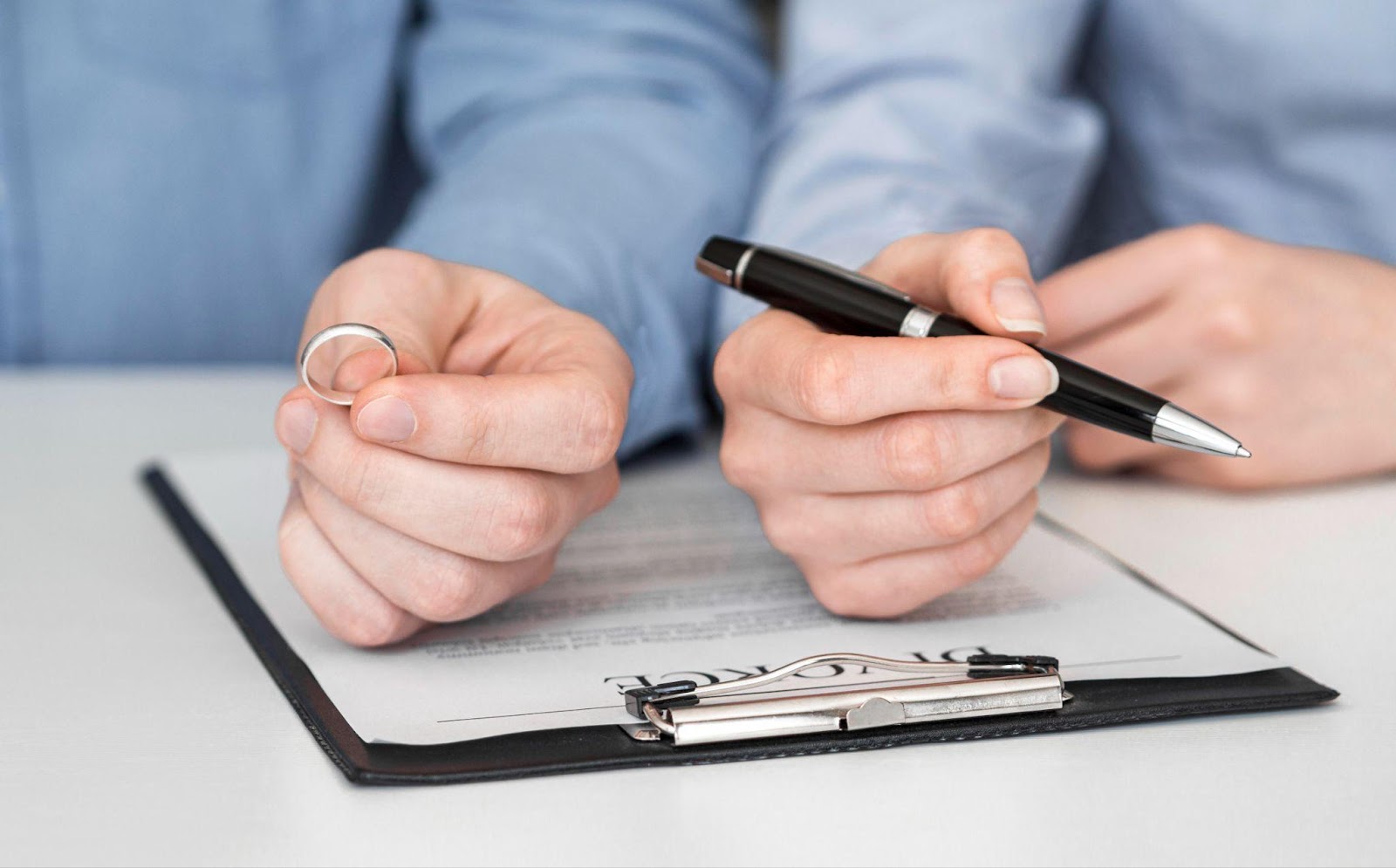 Person holding a wedding ring in one hand and a pen in the other, reviewing divorce paperwork on a clipboard.