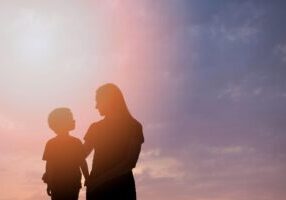 Silhouette of a parent and child standing together against a colorful sunset sky with pink and purple hues, symbolizing the parent-child relationship during transitions like aging out of child support obligations.