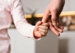 Parent and child holding hands, with a small child's hand grasping an adult's finger, symbolizing parental support and the parent-child relationship in a custody or child support context.