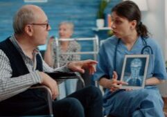 A doctor shows a patient a brain scan on a tablet, explaining details about a brain injury, with the scan highlighting affected areas.