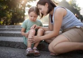 A mother tending to her child's injured knee on the side of a road, symbolizing care after an accident. This image relates to child injury claims, emphasizing the legal rights and compensation available for minors injured due to negligence.