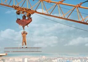 A construction worker operates at a height on a crane, emphasizing the potential risks associated with crane accidents.