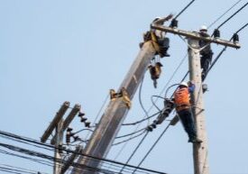 Construction workers are performing tasks on elevated electrical poles, highlighting the risks of electrocution and the importance of adhering to electrical safety regulations.