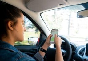 A person checking Google Maps on a smartphone while driving, highlighting the dangers of GPS and navigation system distractions in the context of distracted driving.