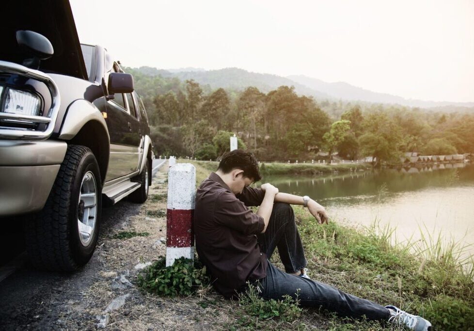 A drunk driver sitting beside his crushed car after a crash, with visible signs of alcohol-related impairment. The scene highlights the serious consequences of drunk driving accidents, including alcohol-related injuries and fatalities.