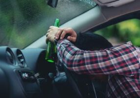 A person drinking from a bottle while driving, highlighting the dangers of drunk driving and the DUI laws and criminal charges enforced in Alabama.