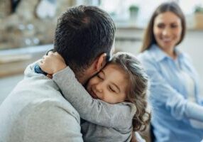 A family with a child hanging onto one parent's arm, symbolizing love and support, with a focus on FAQs about adoption in Alabama. The image highlights the importance of understanding the adoption process and what families need to know when considering adoption in Alabama.