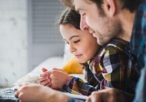 A father and daughter share a tender moment while reading together, symbolizing the importance of child support modifications in Alabama to ensure children's needs are met.