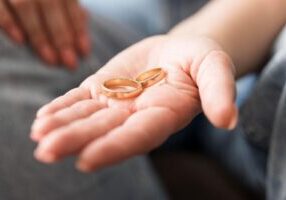 A close-up of a hand holding wedding rings, symbolizing the end of a marriage, with a focus on FAQs about divorce mediation in Alabama. The image highlights the emotional aspect of divorce while providing insight into the mediation process in Alabama.