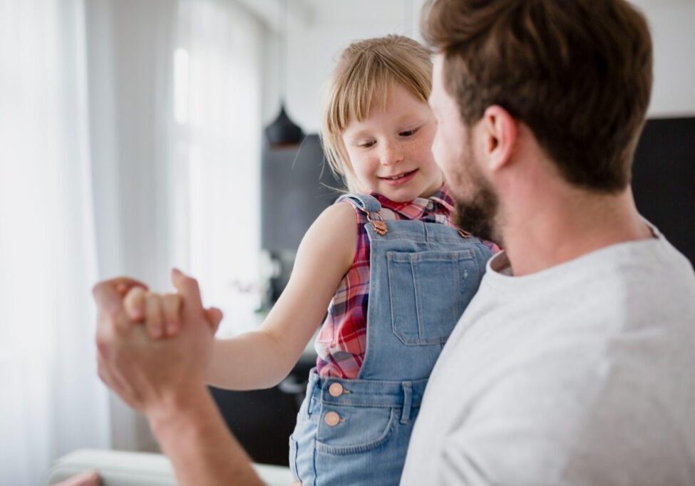 A father joyfully holding his daughter as she hangs playfully from his arms, representing the bond between father and child. The image highlights the topic of FAQs about fathers' rights in Alabama, emphasizing paternal involvement and legal rights.