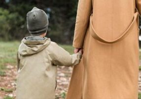 A rear view of a woman holding her child’s hand while walking outdoors, symbolizing the importance of preparing thoroughly for a child custody hearing in Alabama to safeguard the parent-child bond.