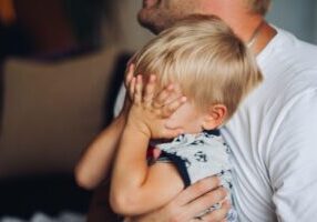 Father holding a young blond child who is covering his face with his hands, illustrating the emotional aspects of custody cases.