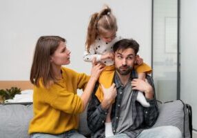 A playful family moment featuring a father with his daughter sitting on his shoulders as the mother adjusts her.