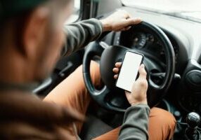 A person checking their phone while driving, illustrating the risks and legal consequences associated with distracted driving and liability determination in Alabama.