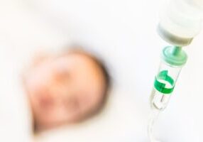 A newborn baby lies in a hospital bassinet, with medical equipment visible in the background. The image highlights concerns surrounding birth injuries and the potential for medical malpractice in neonatal care.