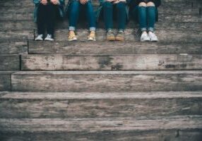 A row of teenagers sitting on concrete steps. The Atmosphere is dull and grey.