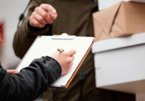 A person’s hand is shown signing a product return form, with the product nearby. The image highlights considerations of product liability, emphasizing the importance of accountability and consumer rights in cases of defective or unsafe products.