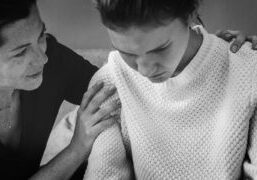 A black-and-white image showing a woman offering support to a younger person in distress. This visual represents the emotional challenges individuals face during difficult times, emphasizing the importance of empathy and understanding in family or interpersonal relationships.