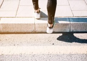 An image showing a person's legs stepping onto a sidewalk, representing the potential hazards of poorly maintained sidewalks. It highlights issues like slip and fall accidents, property upkeep, and legal liability related to pedestrian safety.