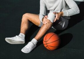 An athlete sitting on the court holding a knee injury, highlighting the discussion of sports injuries, including the liability of coaches, teams, and sports facilities in Alabama.