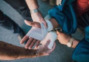 Concerned bystanders helping an injured pedestrian with a bandaged hand after a T-bone accident.