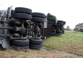 Side view of a truck that has been involved in a severe accident, lying on its side with visible damage from the crash.