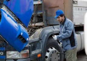 A mechanic examines the tire and engine area of a large truck, possibly checking for damages or maintenance after a truck accident.