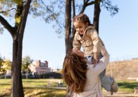 A joyful mother lifting her smiling child in a sunny park, symbolizing the importance of understanding Alabama child custody laws to prioritize a child’s well-being and happiness.