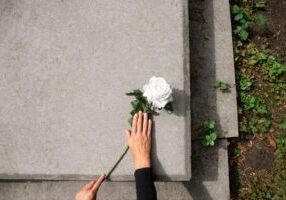 A hand gently places a flower on a tombstone, symbolizing remembrance and loss. The image conveys the sorrow associated with wrongful death claims, emphasizing the pursuit of justice for a loved one's untimely passing due to negligence.